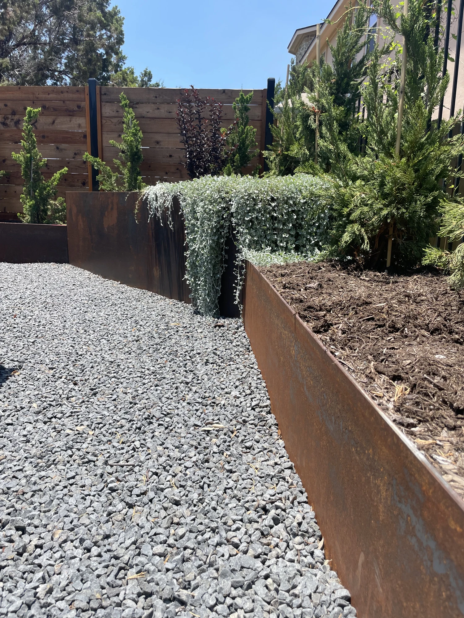 Custom steel planters with layered planting beside a gravel garden path